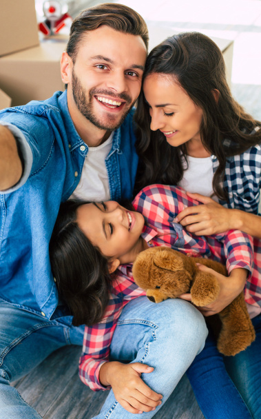 Genç bir baba, anne ve kız ailesi yeni bir dairede yerde oturmuş gülüyor ve birlikte selfie çekiyorlar.. - Fotoğraf, Görsel