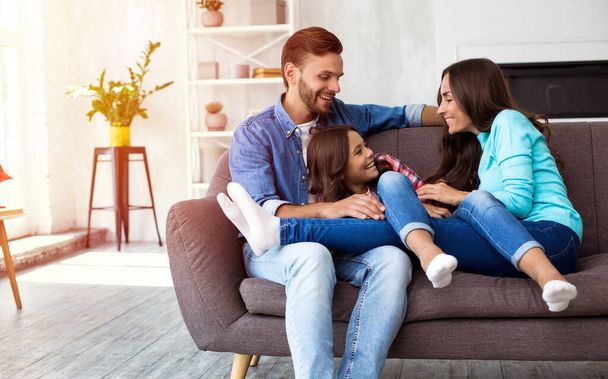 Happy young parents with a little daughter on sofa in their apartment  - Foto, imagen
