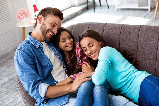 Happy young parents with a little daughter on sofa in their apartment  - Foto, Imagem