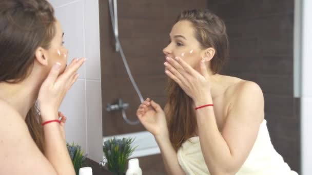 Mujer aplicando crema a la piel mientras que el maquillaje facial en el espejo en el baño
. - Imágenes, Vídeo