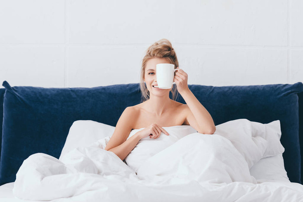 beautiful emotional woman with cup of coffee sitting in bed in morning  - Фото, зображення