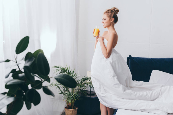 happy girl with glass of juice in white sheets in bedroom in morning - Zdjęcie, obraz