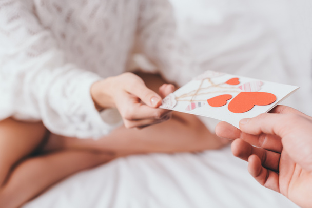 recortado vista de la mujer tomando tarjeta de felicitación con corazones para el día de San Valentín de hombre en la cama
 - Foto, imagen