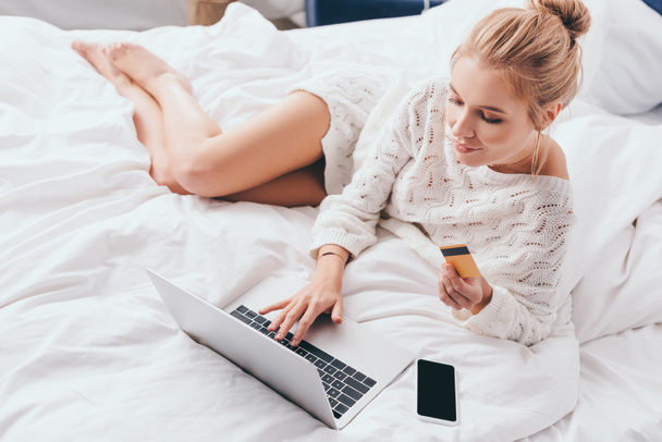 atractiva mujer de compras en línea con ordenador portátil y tarjeta de crédito en la cama por la mañana
  - Foto, Imagen
