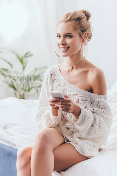 beautiful smiling woman using smartphone on bed in morning  - Φωτογραφία, εικόνα