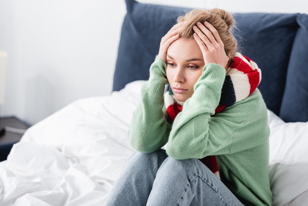 mujer enferma en suéter y bufanda con dolor de cabeza sentado en la cama
 - Foto, Imagen