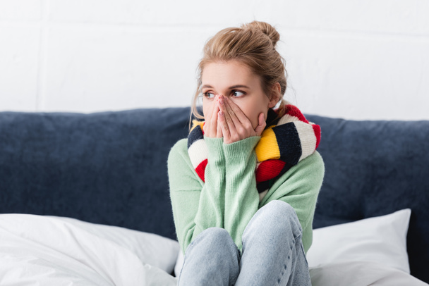 giovane donna malata in maglione e sciarpa seduta sul letto
  - Foto, immagini