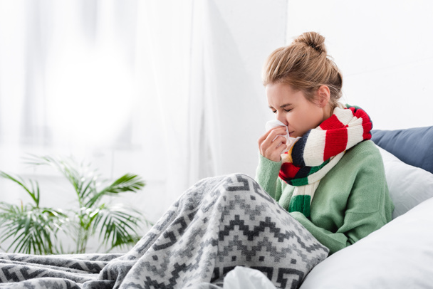 sad ill woman in scarf having runny nose in bed with napkins - Zdjęcie, obraz