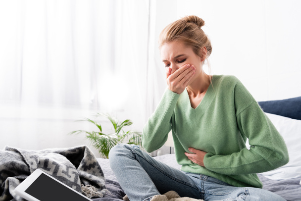 woman having nausea and sitting on bed with digital device - Photo, Image