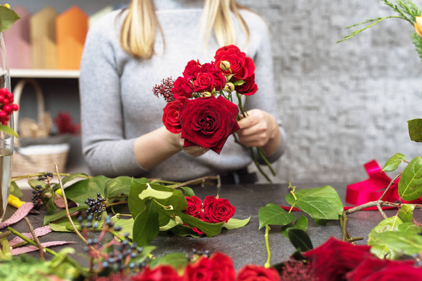A beautiful girl collects a dark bouquet of burgundy red roses in her studio. Male florist creating beautiful bouquet in flower shop. Flowers delivery, creating order, Small business - Zdjęcie, obraz