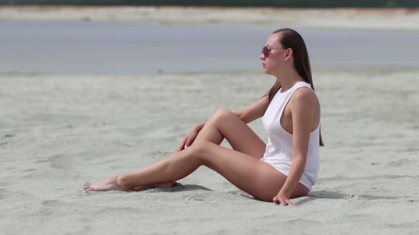 Languid femme assise jambes croisées sur sable toucher la peau
 - Séquence, vidéo
