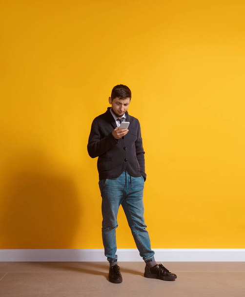 Young caucasian man using smartphone. Full body length portrait isolated over yellow background. - Fotó, kép