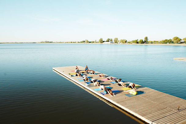 A nagy csoport az emberek részt jóga osztályok egy ponton, közel a tó. - Fotó, kép