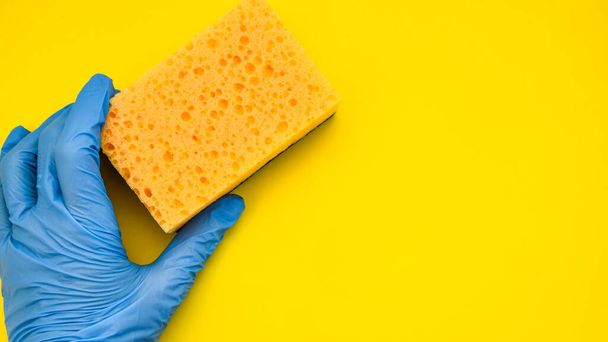 Limpeza geral, mão em borracha com esponja no fundo amarelo, espaço de cópia
 - Foto, Imagem