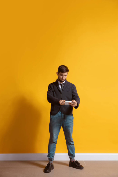 Young caucasian man using smartphone. Full body length portrait isolated over yellow background. - Foto, imagen
