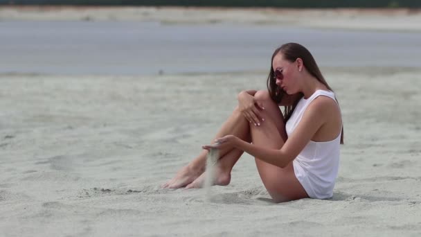 Mujer lánguida sentada con las piernas cruzadas sobre la arena tocando la piel
 - Imágenes, Vídeo