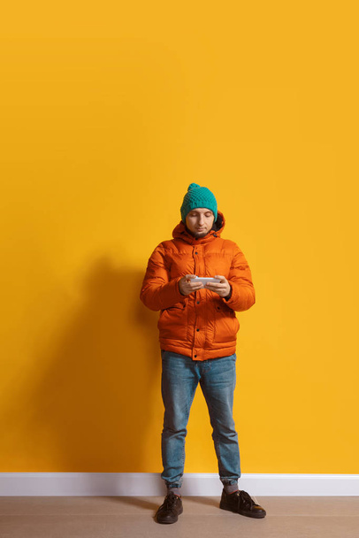 Young caucasian man using smartphone. Full body length portrait isolated over yellow background. - Fotoğraf, Görsel