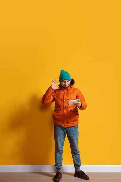 Young caucasian man using smartphone. Full body length portrait isolated over yellow background. - Photo, Image
