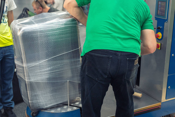 Werknemer wikkelen koffer met transparante beschermfolie op luchthaven vertrekterminal voor de vlucht. Bagagebescherming en veiligheidsdienst - Foto, afbeelding