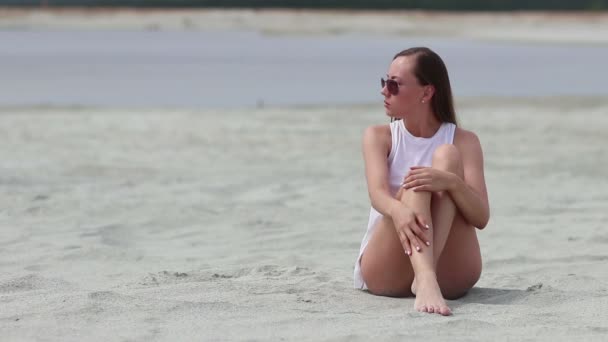 Νωθρή γυναίκα κάθεται με σταυρωμένα πόδια στην άμμο αγγίζοντας το δέρμα - Πλάνα, βίντεο