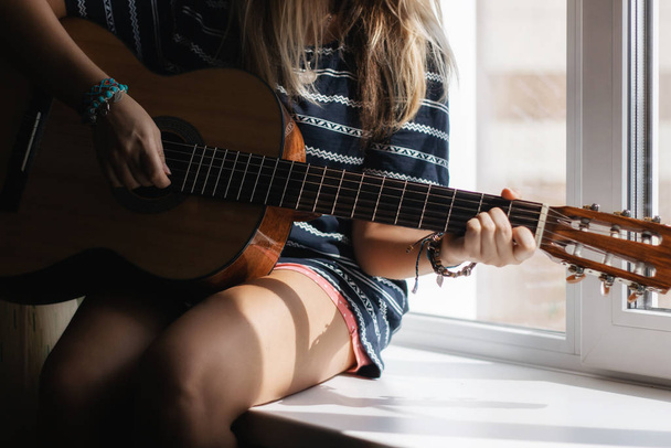 cropped shot of woman in striped dress playing guitar on windowsill - Foto, Bild