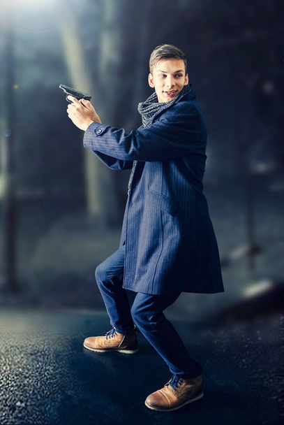 Man in coat and scarf pointing gun, armed robbery at night or contract killing, - Foto, immagini