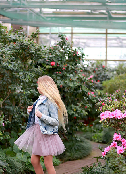girl with long white hair in a denim jacket walks in a flowering - Zdjęcie, obraz