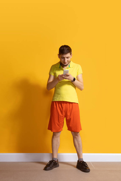 Homem caucasiano jovem usando smartphone. Retrato de corpo inteiro isolado sobre fundo amarelo
. - Foto, Imagem