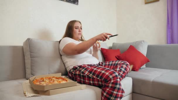 Frau mit Übergewicht isst Pizza und schaut fern - Filmmaterial, Video