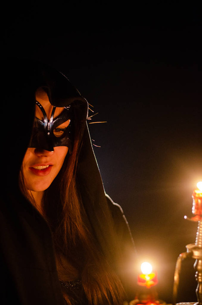 misteriosa jovencita vestida con una capa negra, sábado de brujas en el bosque por la noche junto a la hoguera - Foto, Imagen