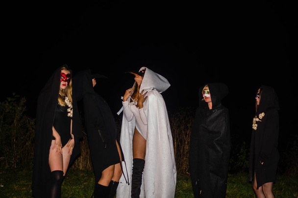 таємничі молоді дівчата в чорно-білих плащах, субота відьми в лісі вночі біля багаття
 - Фото, зображення