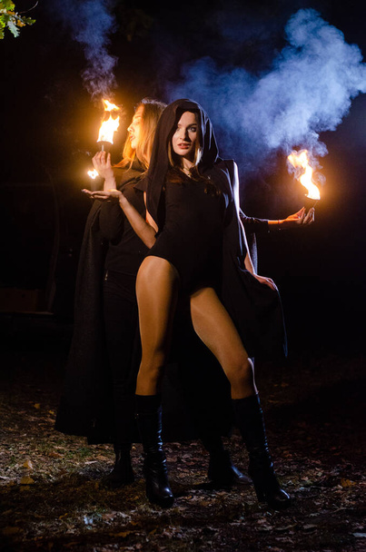 mystérieuses jeunes filles portant des manteaux noirs, sabbat de sorcière dans les bois la nuit près du feu de joie - Photo, image