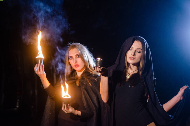 mystery young girls wearing black cloaks, witch's sabbath in the woods at the night by the bonfire - Photo, Image