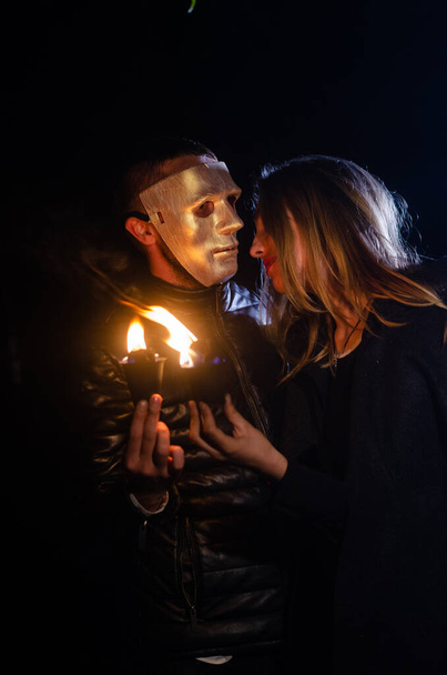 mystère jeune fille portant manteau noir et homme masqué, sabbat de sorcière dans les bois la nuit près du feu de joie - Photo, image