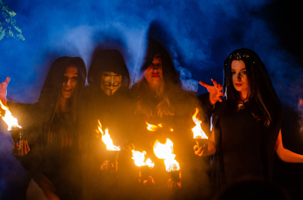 mystérieux jeunes filles et homme portant des manteaux noirs, sabbat de sorcière dans les bois la nuit près du feu de joie - Photo, image