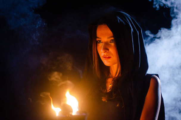 rejtélyes fiatal lány fekete köpenyt visel, boszorkány szombat az erdőben éjszaka a máglya mellett - Fotó, kép