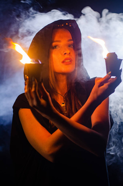 Mysteriöses junges Mädchen in schwarzem Mantel, Hexensabbat im Wald in der Nacht am Lagerfeuer - Foto, Bild