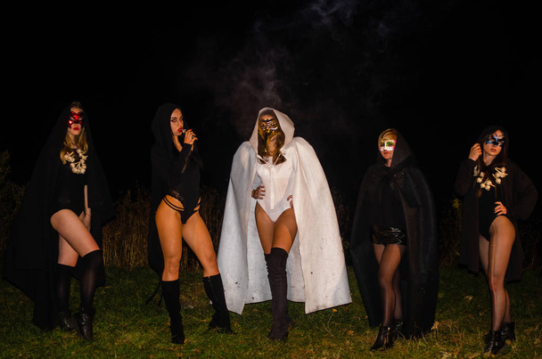 загадочные девушки в черно-белых плащах, шабаш ведьм в лесу ночью у костра - Фото, изображение
