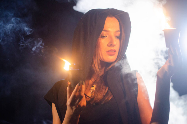 mysterie jong meisje draagt zwarte mantel, heks sabbat in het bos 's nachts bij het kampvuur - Foto, afbeelding