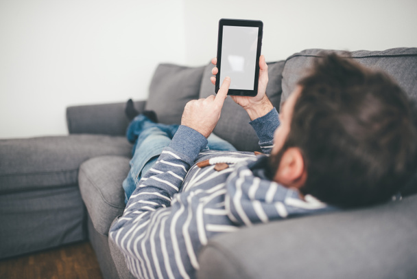 man using small digital tablet or ebook reader while relaxing on sofa - Fotó, kép