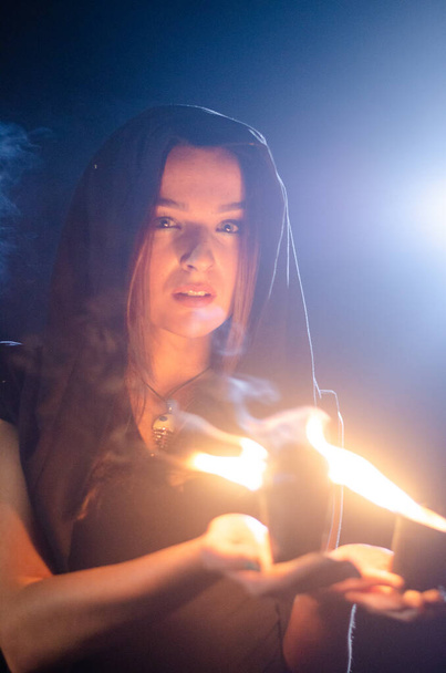 jovem misteriosa vestindo manto preto, sábado de bruxa na floresta à noite perto da fogueira - Foto, Imagem