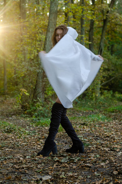 sexy young girl wearing white bodysuit and cloak posing in the forest - Foto, Imagen