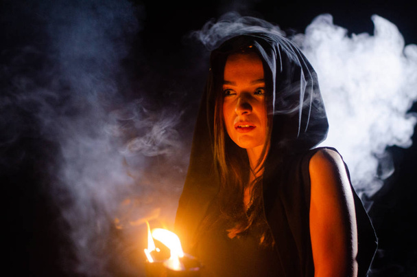 Mysteriöses junges Mädchen in schwarzem Mantel, Hexensabbat im Wald in der Nacht am Lagerfeuer - Foto, Bild