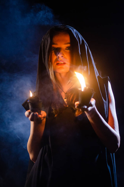 mystérieuse jeune fille vêtue d'un manteau noir, sabbat de sorcière dans les bois la nuit près du feu de joie - Photo, image