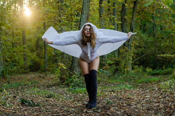 sexy jong meisje dragen witte bodysuit en mantel poseren in het bos - Foto, afbeelding