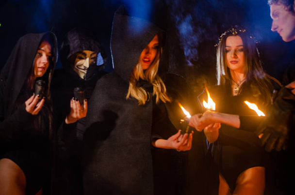 mistério meninas e homem vestindo capas pretas, sábado de bruxa na floresta à noite, perto da fogueira - Foto, Imagem