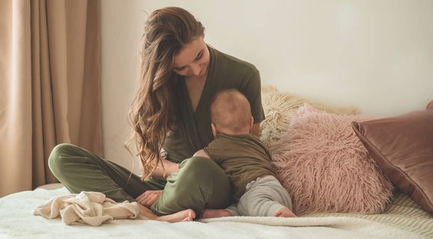 ベッドの上で母親と赤ちゃんの男の子の家の肖像画。ママは子供とキスしてる第一歩. - 写真・画像