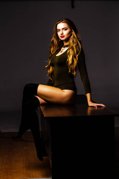 Beautiful dancer. Girl model. the girl sits in a hat and sits on a table. girl in a beautiful underwear. the girl is sitting on the table and fooling around, making faces. smooth, well-groomed legs - Photo, Image