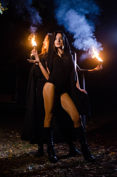 mystérieuses jeunes filles portant des manteaux noirs, sabbat de sorcière dans les bois la nuit près du feu de joie - Photo, image