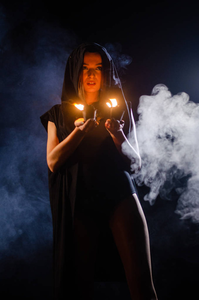 mystérieuse jeune fille vêtue d'un manteau noir, sabbat de sorcière dans les bois la nuit près du feu de joie - Photo, image